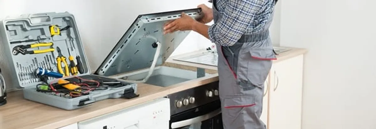 Cooktop repair technician lifting a built-in stovetop for service in Glendale, AZ